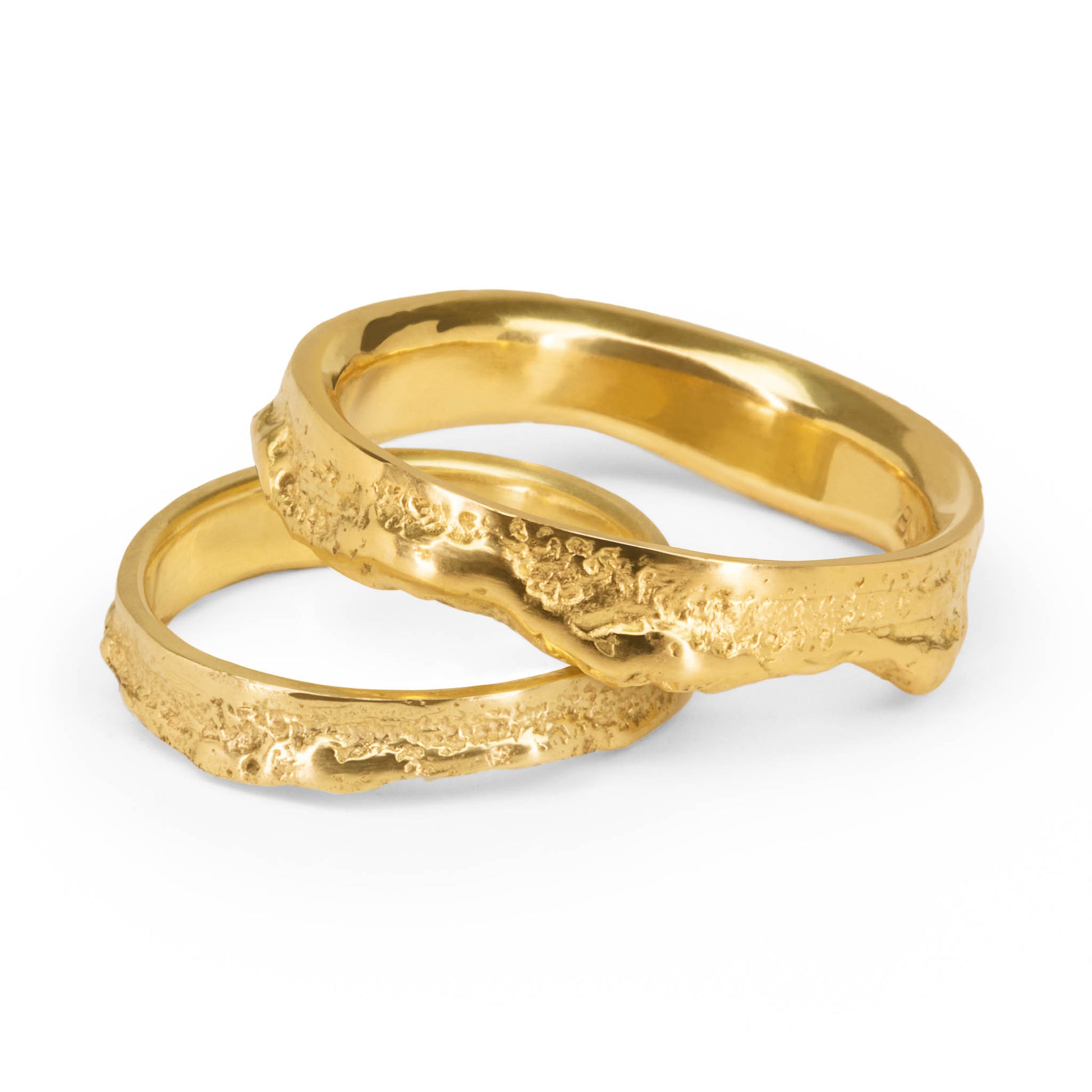 Yellow gold wedding bands with an organic and a straight half on a white background.