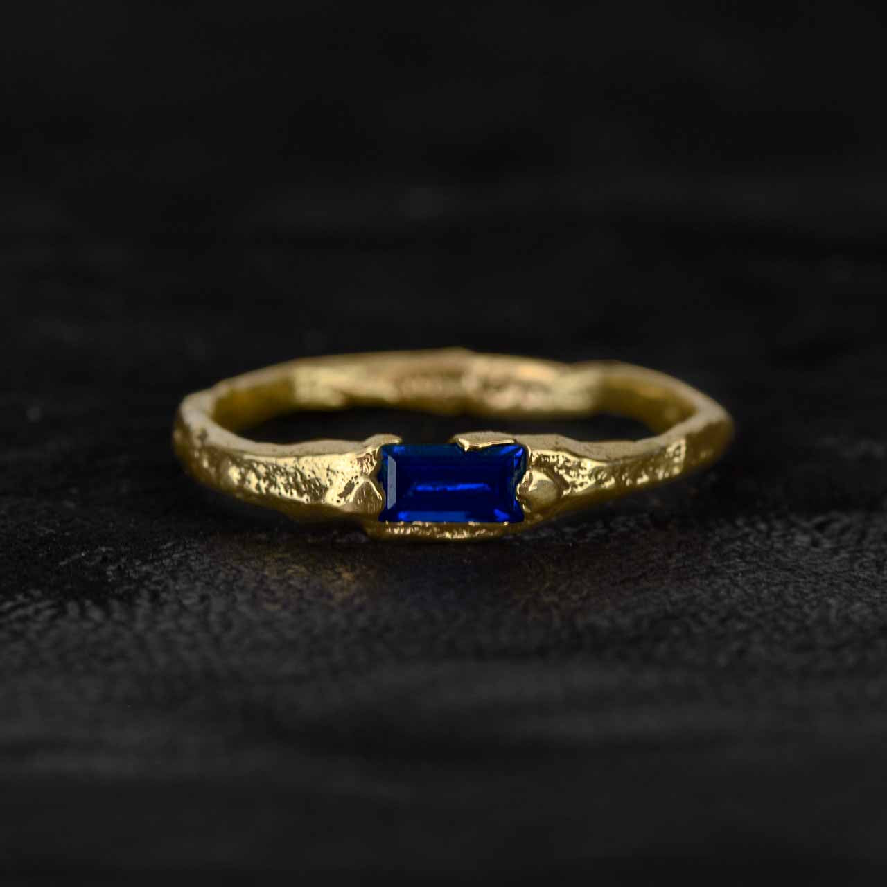 An engagement ring in yellow gold with a blue gemstone on a dark background.