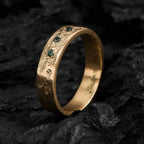 Yellow gold wedding band with an organic texture and three brilliant cut tourmalines standing on a dark background.