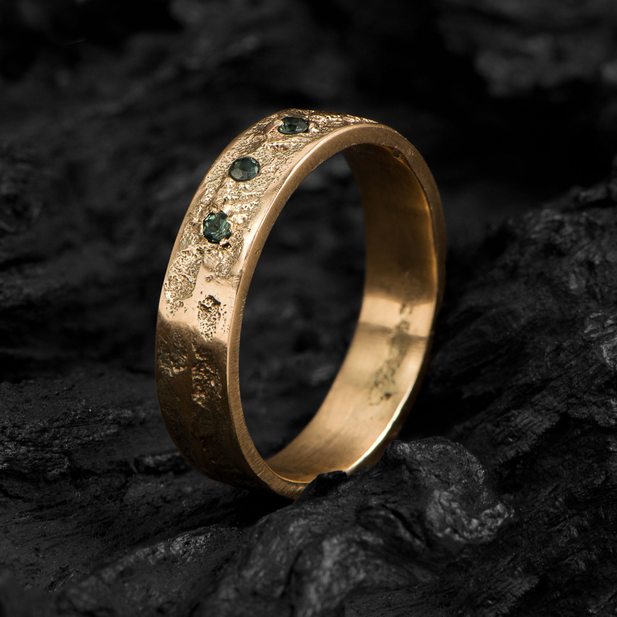 Yellow gold wedding band with an organic texture and three brilliant cut tourmalines standing on a dark background.
