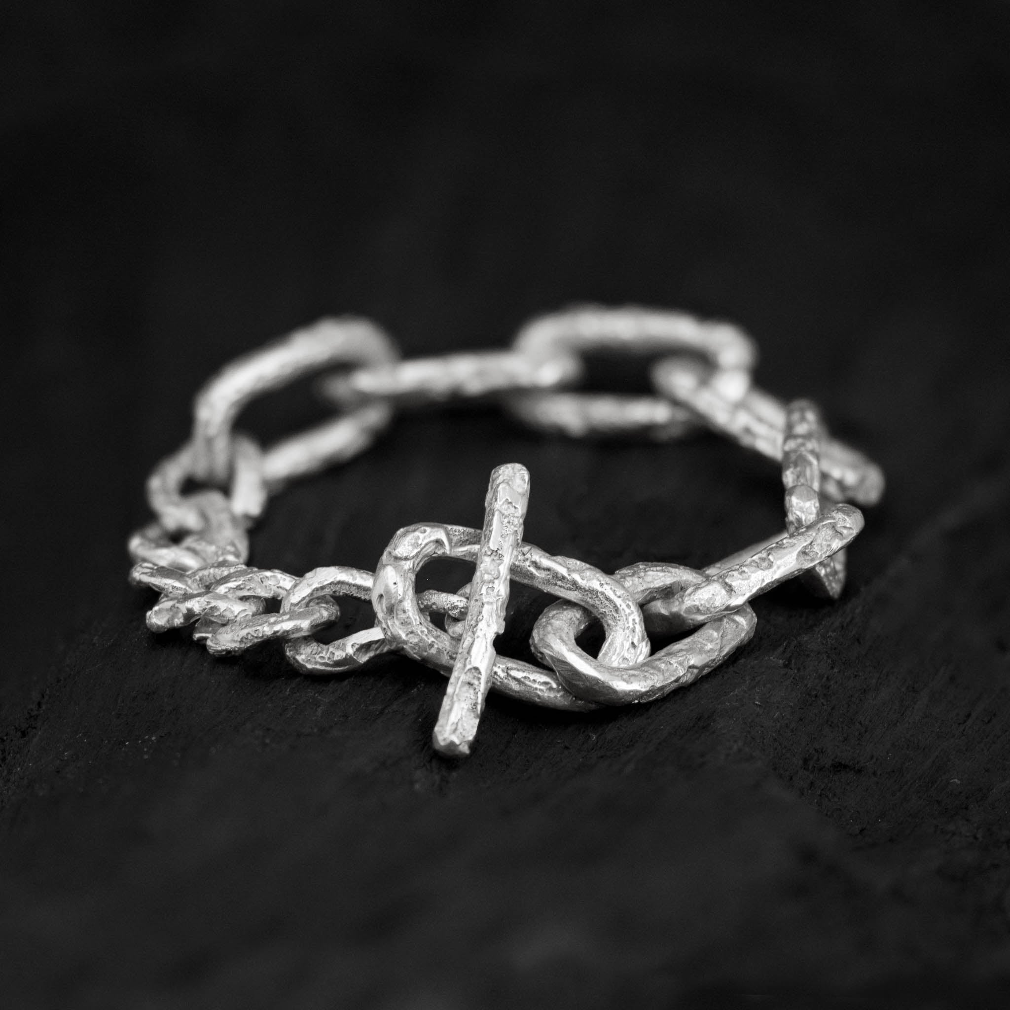 Sterling silver link chain bracelet with a big toggle clasp and lots of texture, handcrafted in Berlin on a dark background.