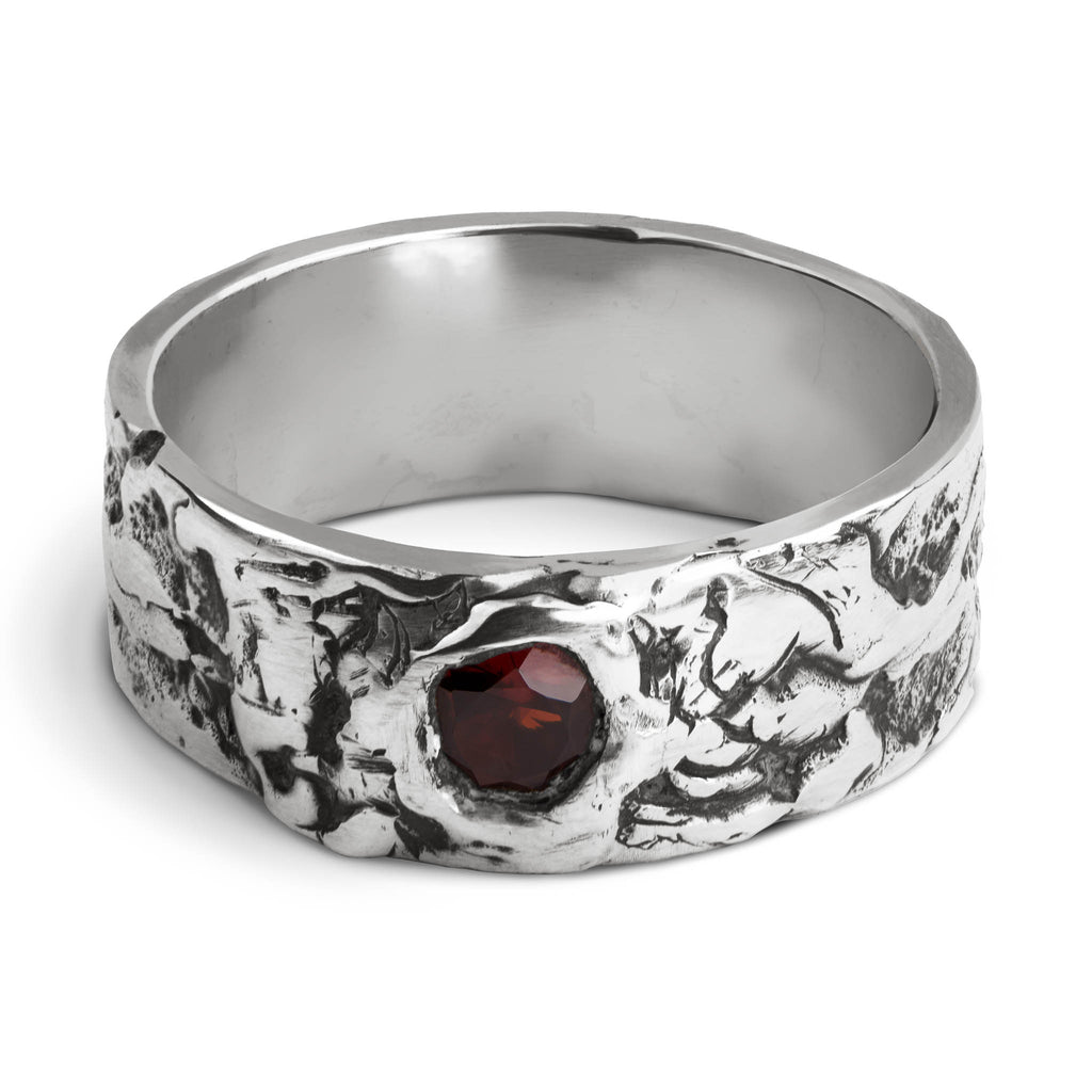 Handcrafted sterling silver ring with a 8 mm textured band and a 5mm brilliant cut garnet set in an organic surface on a white background.