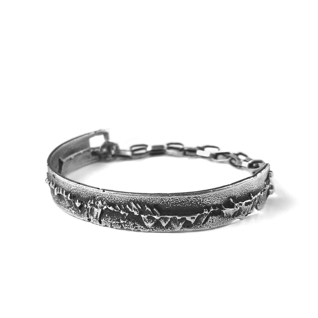 Handcrafted dark silver cuff bracelet with chain closure and a raw edgy surface.