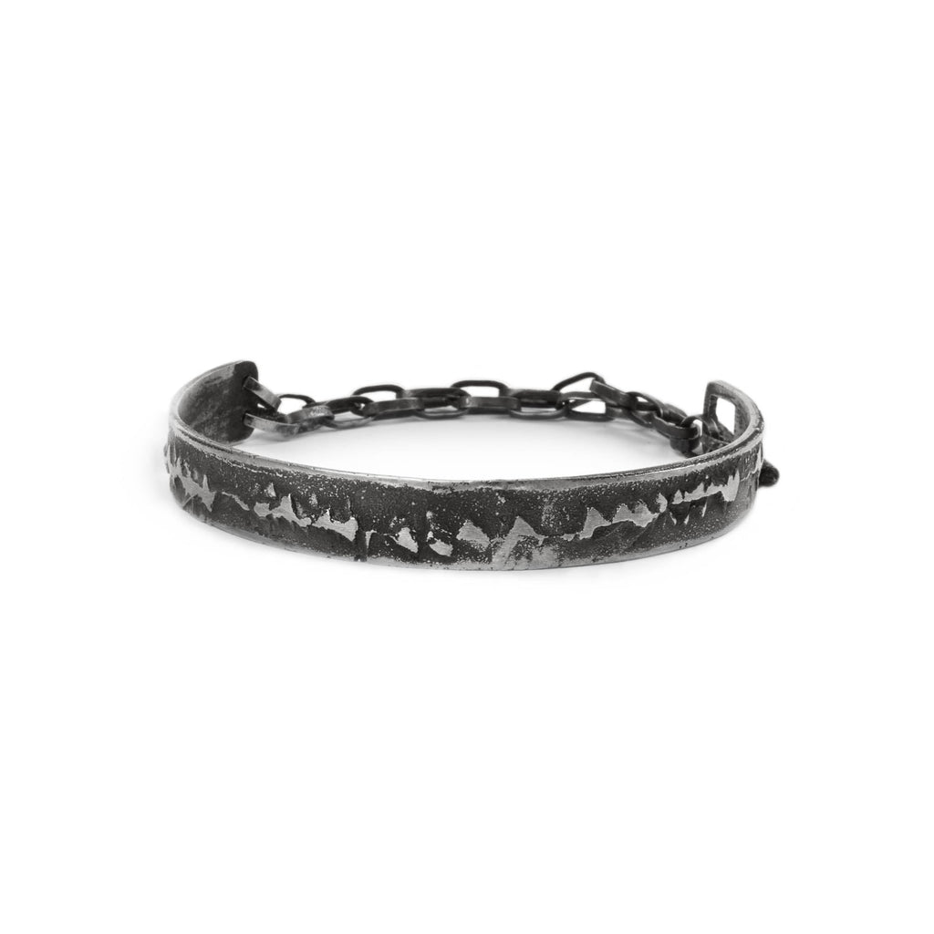 Silver cuff bracelet with texture and chain on a white background