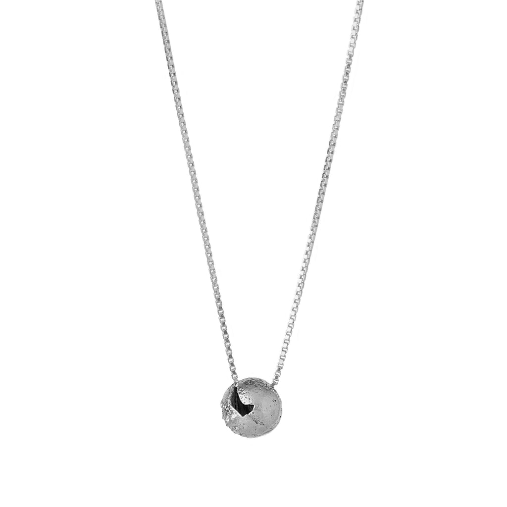 A silver pendant with a spherical shape with craters and a rugged texture suspended from a silver curb chain against a white background.
