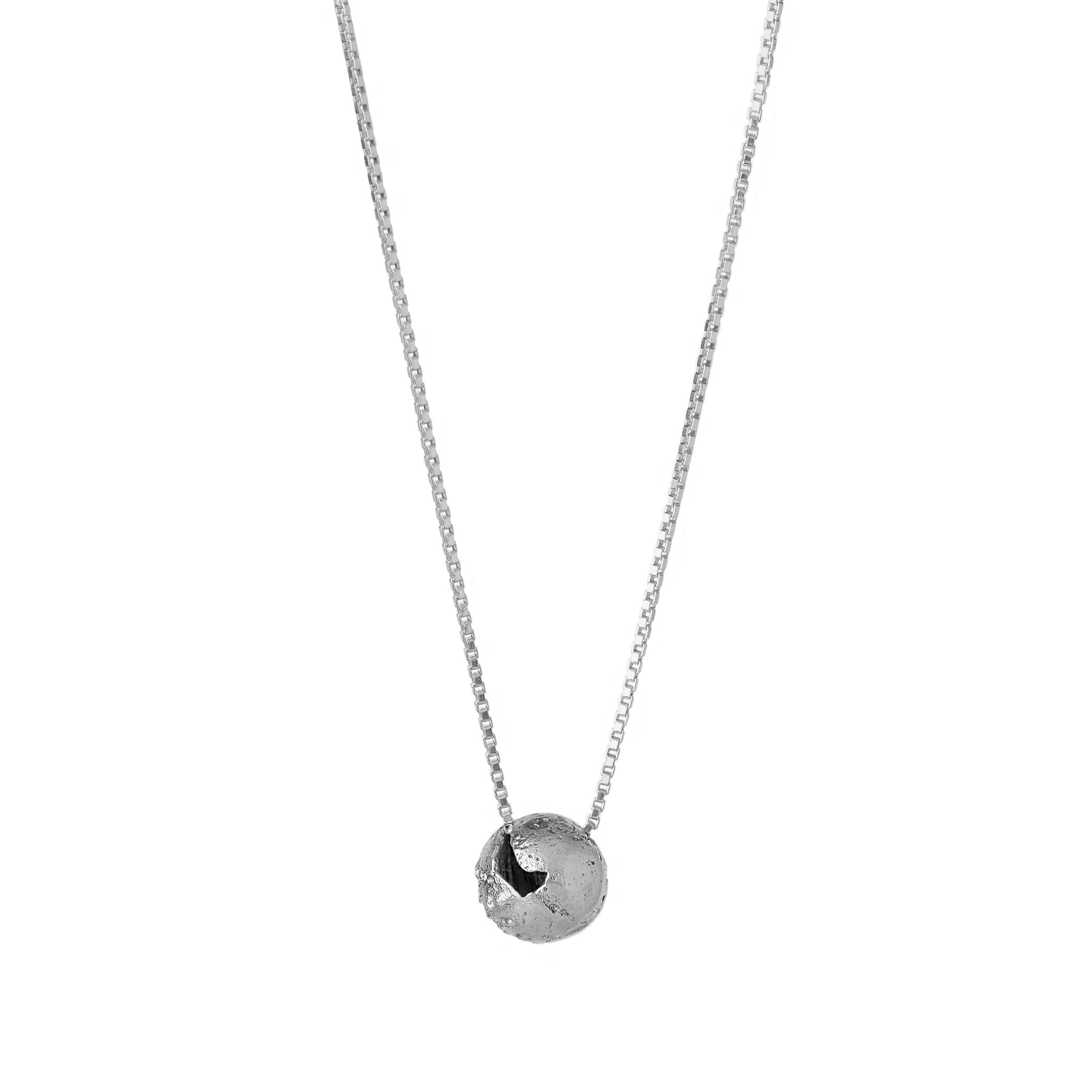 A silver pendant with a spherical shape with craters and a rugged texture suspended from a silver curb chain against a white background.