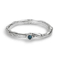 Organic wavy sterling silver ring set with a blue diamond laying on a white background.