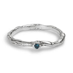 Organic wavy sterling silver ring set with a blue diamond laying on a white background.
