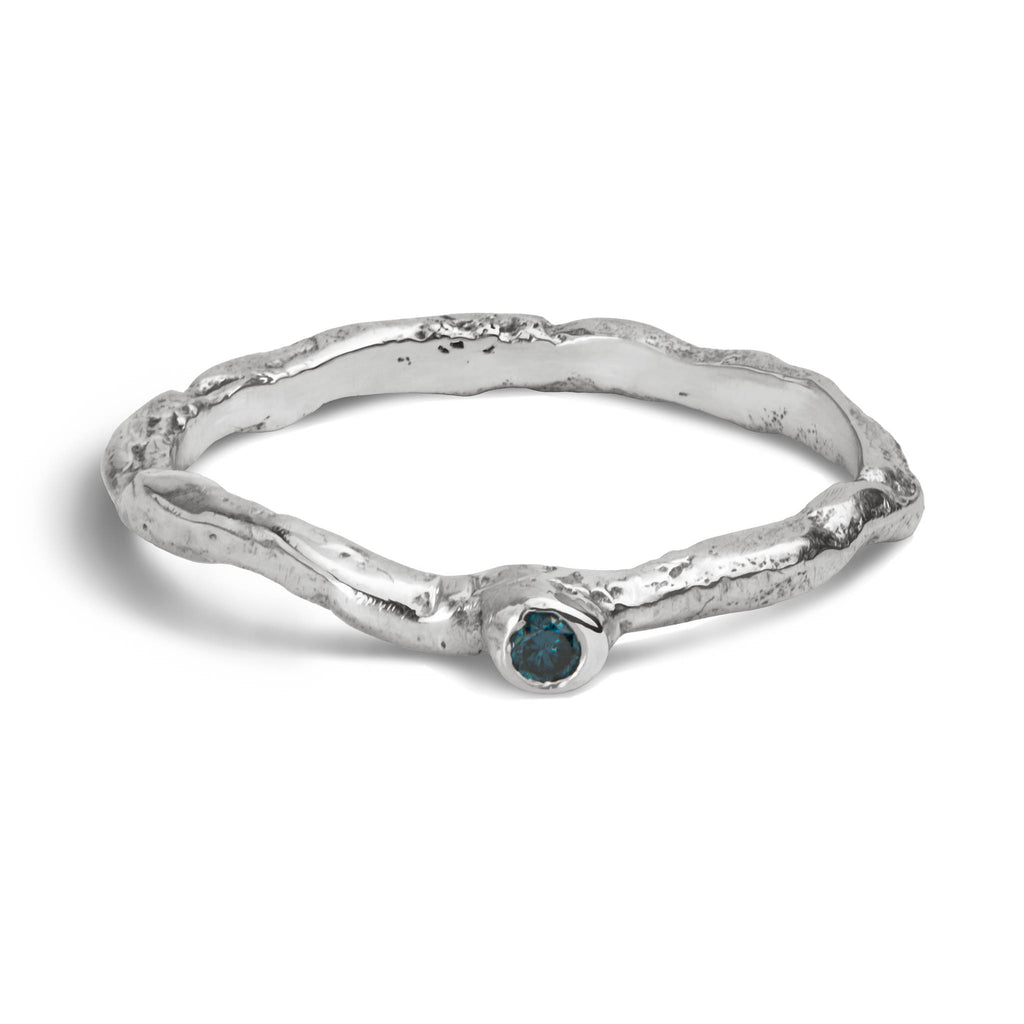 Handcrafted organic textured sterling silver ring set with a blue diamond laying on a white background.
