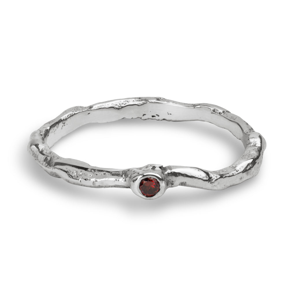 A textured sterling silver ring with a wavy, organic band and a small round red gemstone set in the center, shown on a clean white background.