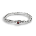 A textured sterling silver ring with a wavy, organic band and a small round red gemstone set in the center, shown on a clean white background.