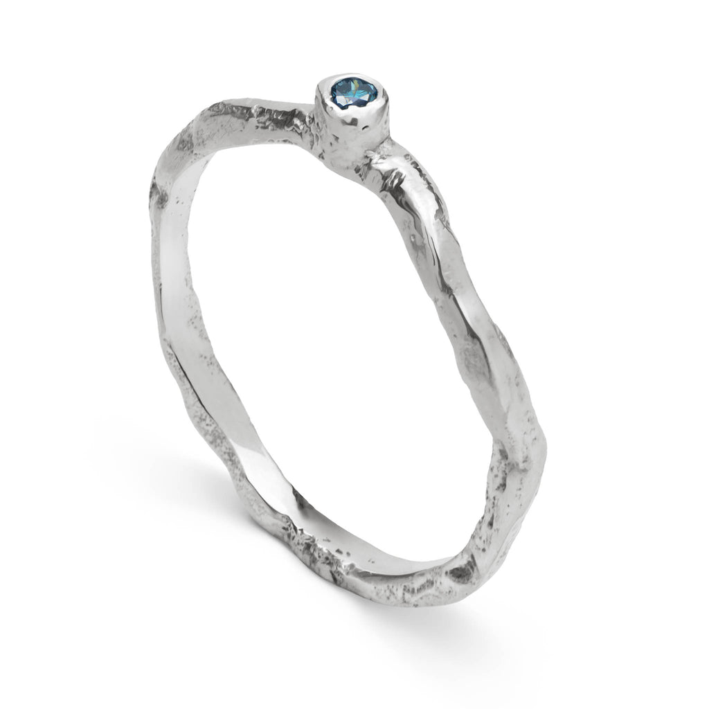 Handcrafted wavy textured sterling silver band set with a blue diamond standing on a white background.