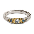 Two tone ring in white gold and yellow gold with one diamond and two blue sapphires in an organic handmade band.