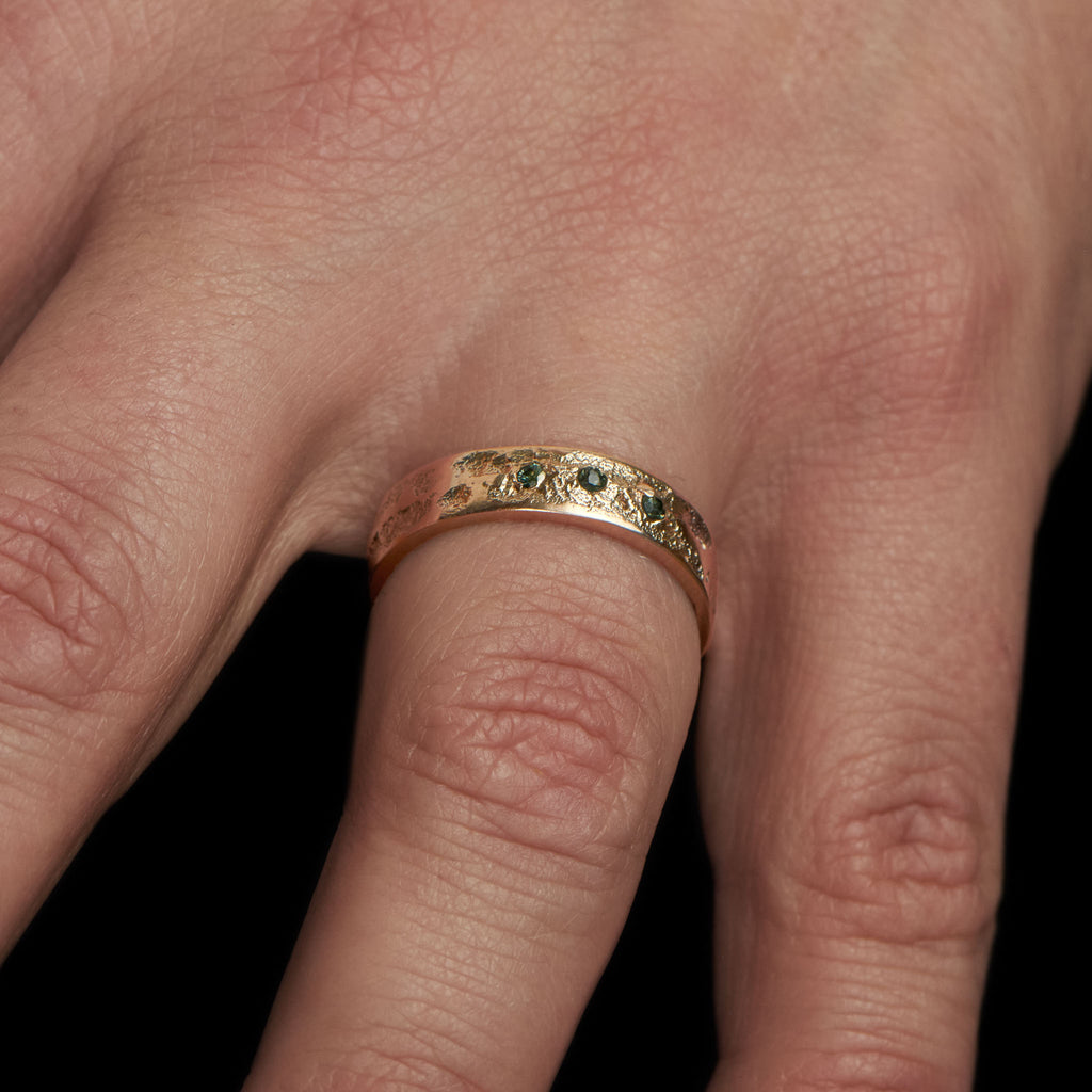 Hand showing a handcrafted gold ring with 3 brilliant cut troumalines.