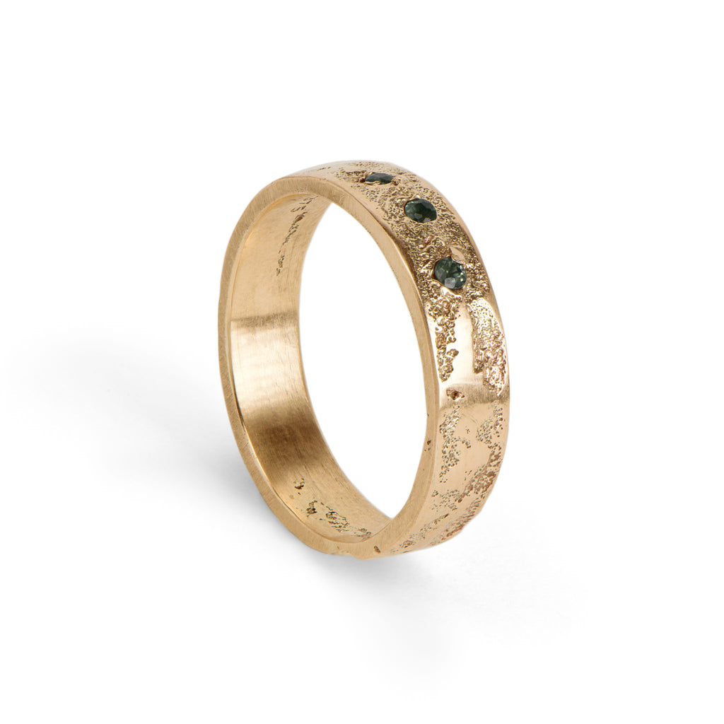 Gold ring with an organic texture ad three green brialliant cut gemstones on a white background.