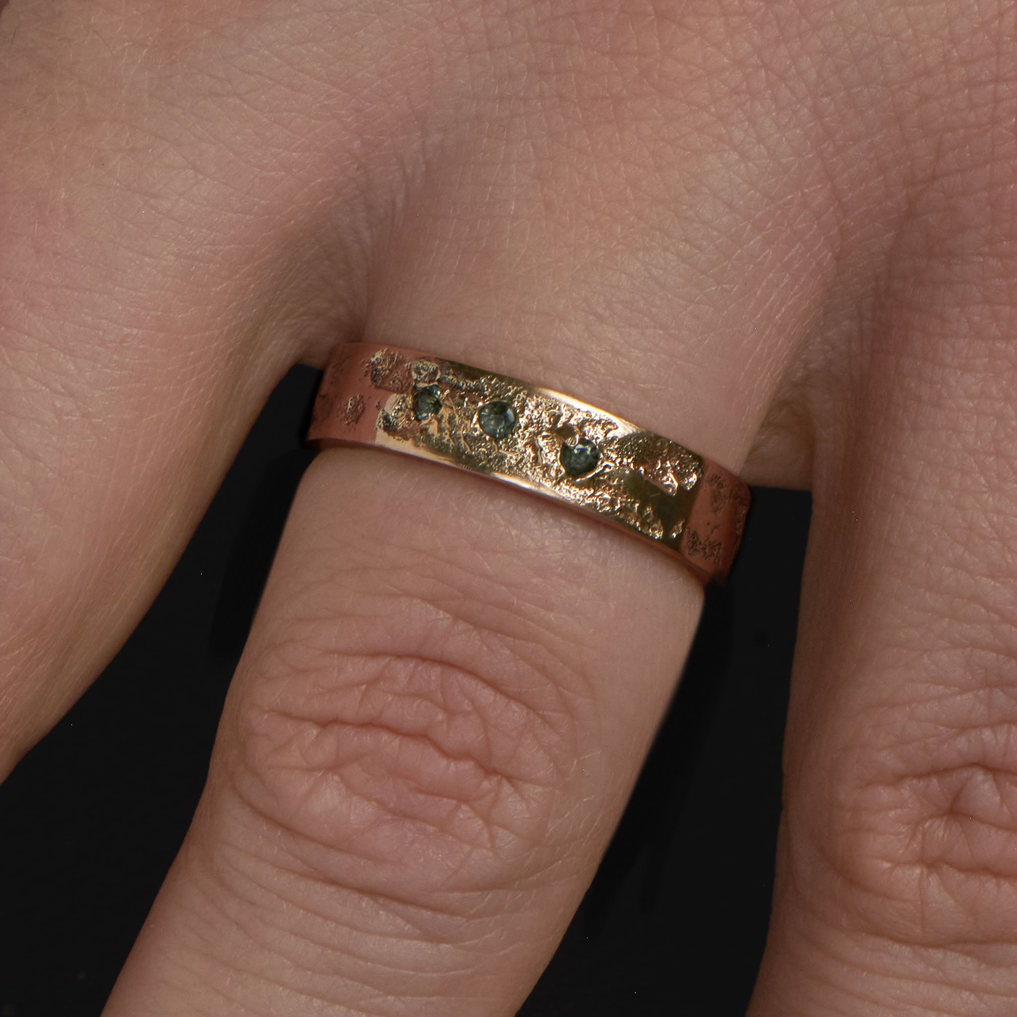 Close up of the Sabik ring in yellow gold with three tourmalines on a finger.
