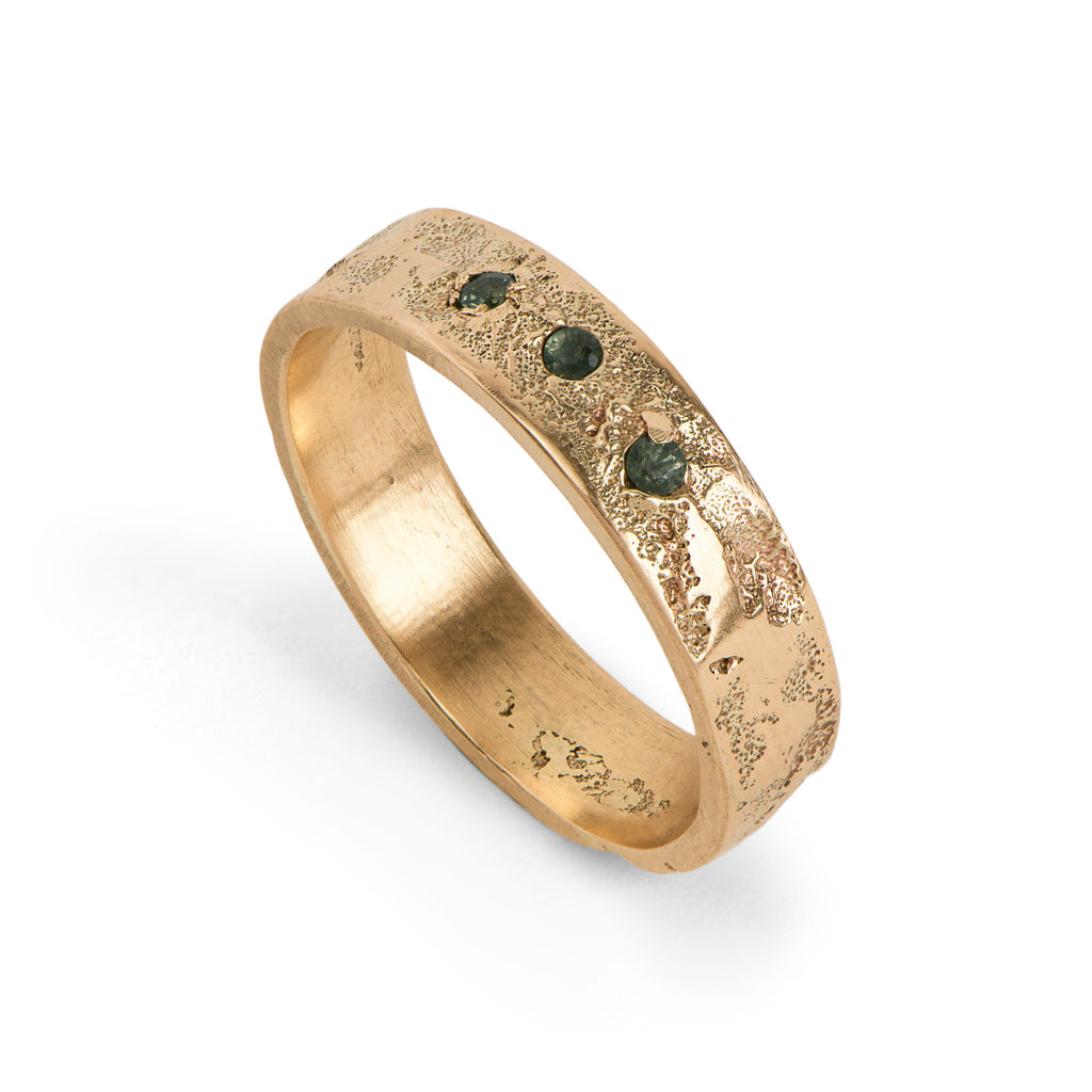 Handcrafted wedding band in yellow gold with three tourmalines standing on a white background.