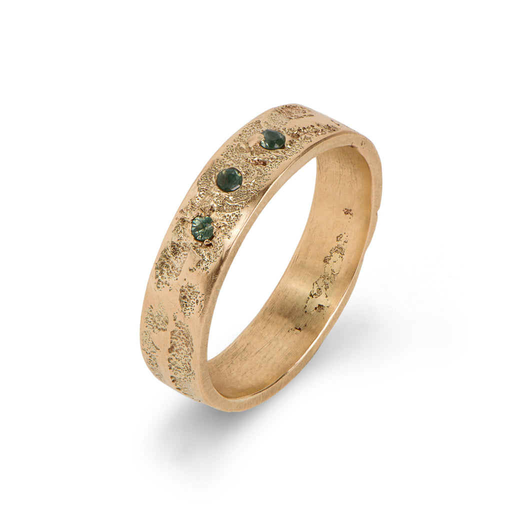 Handcrafted gold ring with three green tourmalines, displayed against a white background.