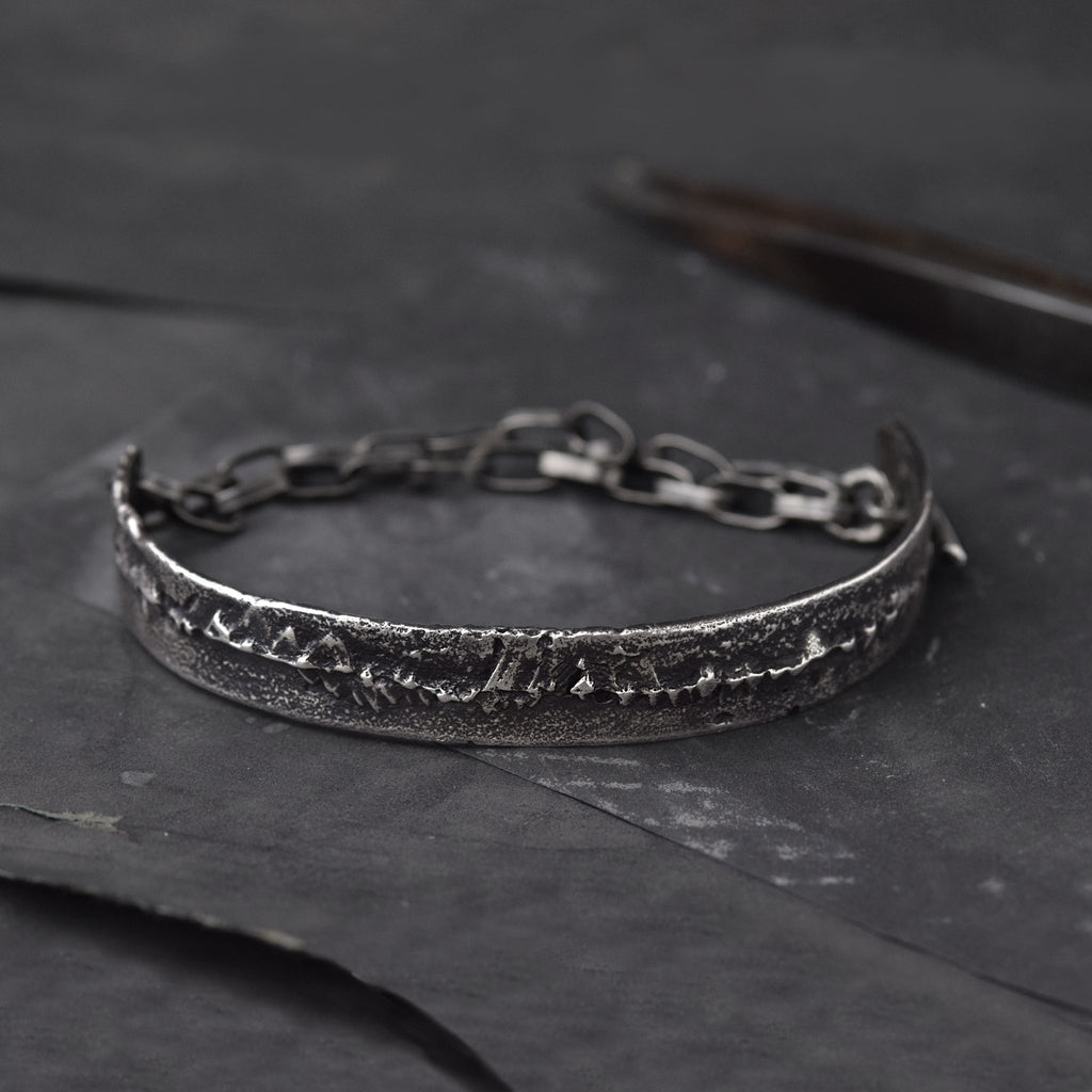 Mens cuff Bracelet in Sterling Silver, laying on a dark surface with some goldsmiths tools.