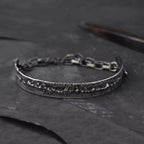 Mens cuff Bracelet in Sterling Silver, laying on a dark surface with some goldsmiths tools.