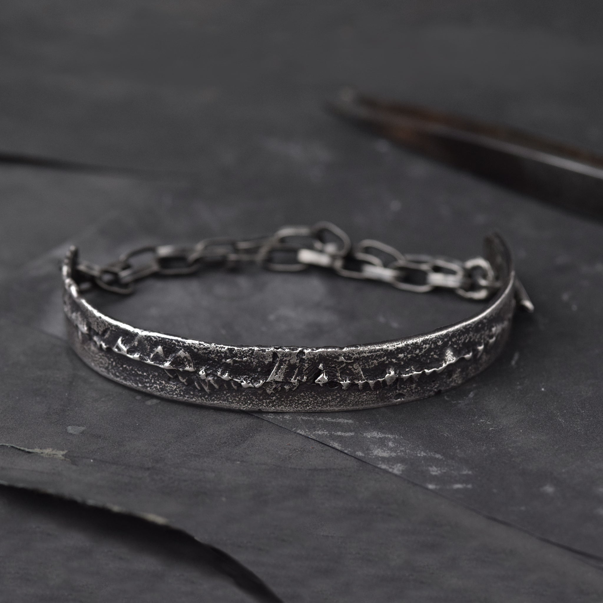 Mens cuff Bracelet in Sterling Silver, laying on a dark surface with some goldsmiths tools.