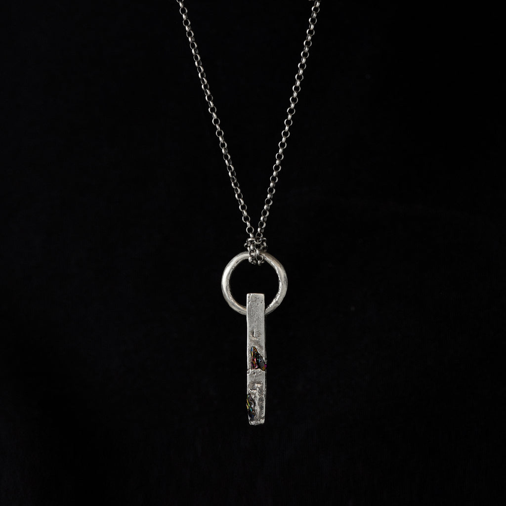 Handcrafted sterling silver necklace with sculptural bar pendant and suspended silver ring on a black bacrground