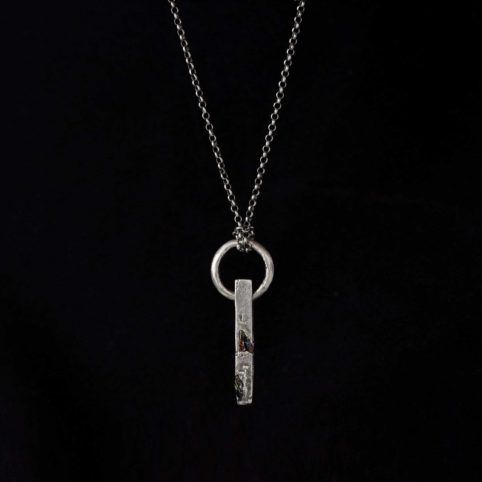 Handcrafted sterling silver necklace with sculptural bar pendant and suspended silver ring on a black bacrground