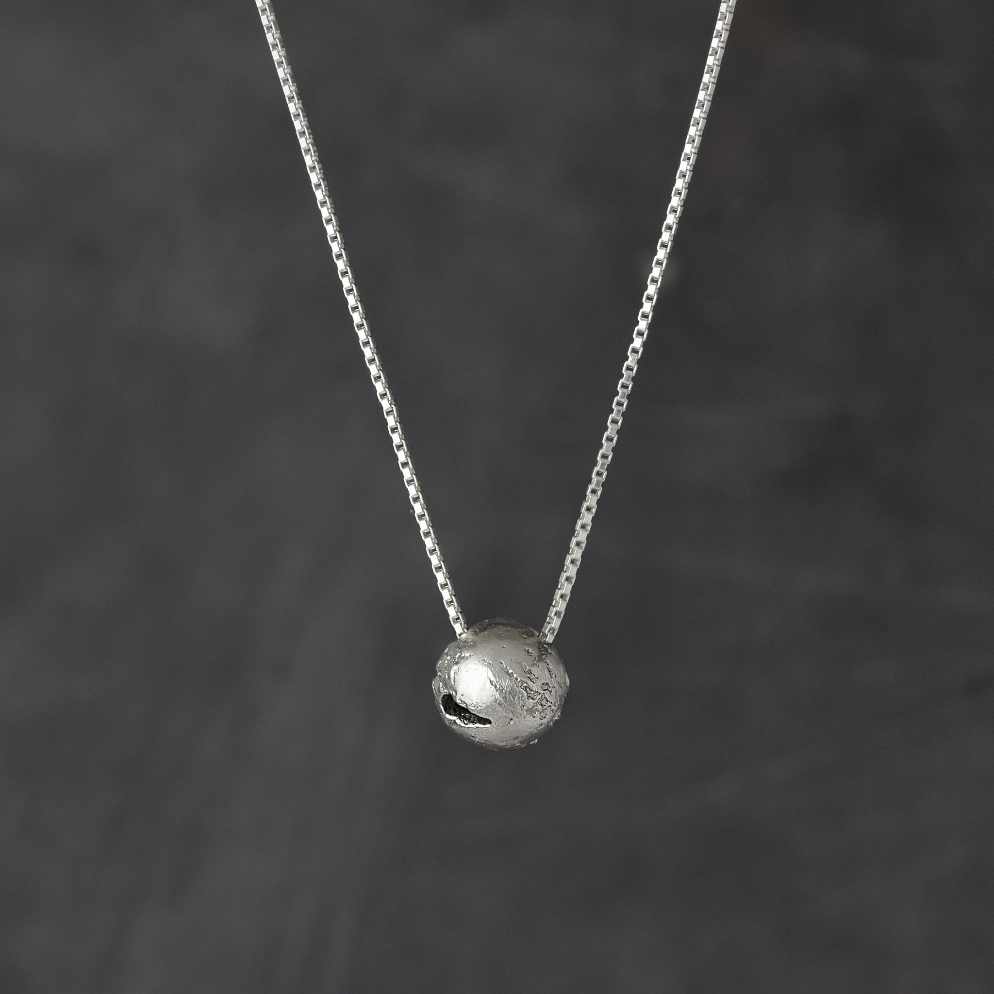 Suspended from a sterling silver chain hangs a handcrafted round pendant reminiscent of earth.