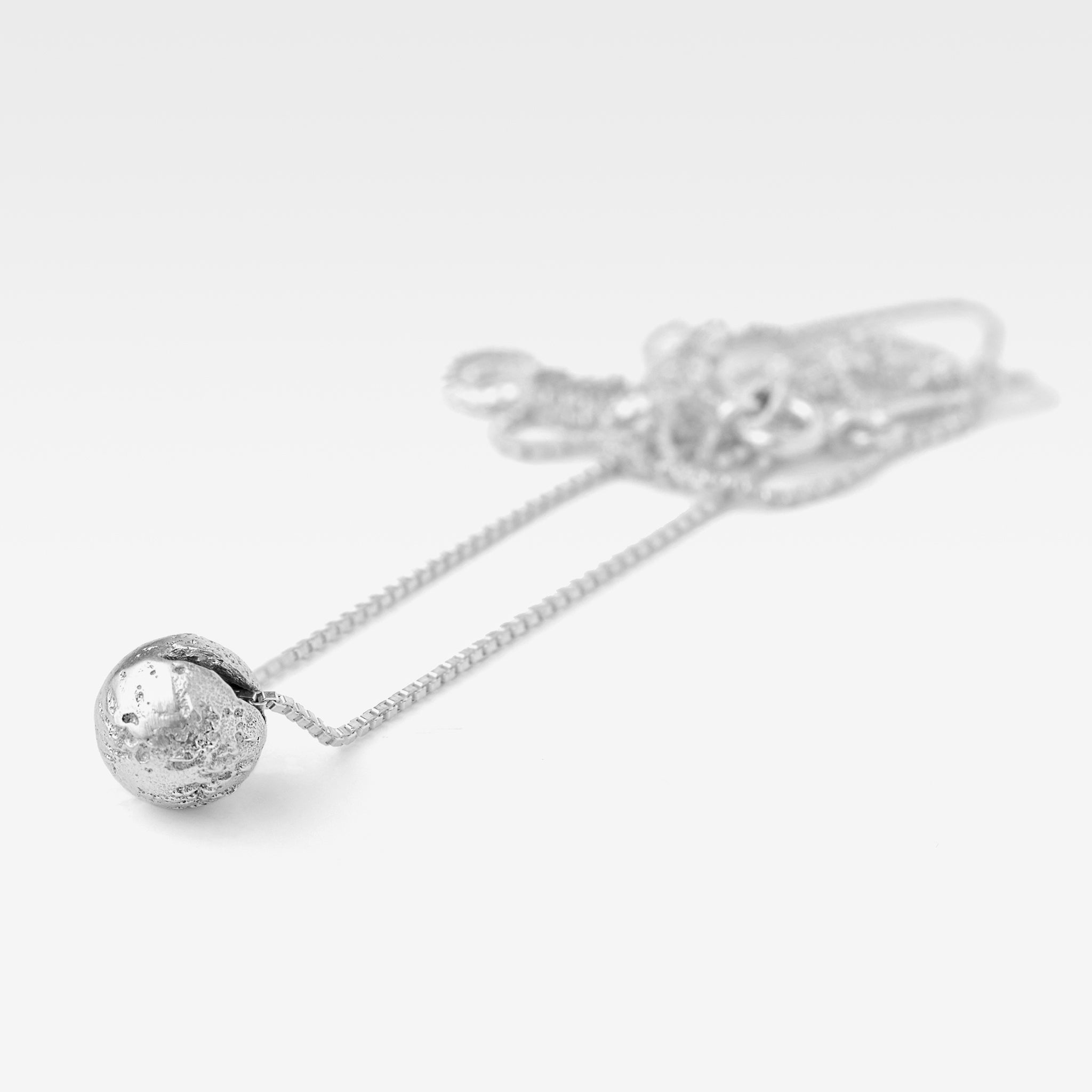 Sterling silver sphere pendant with an earth like texture laying flat on a white background.