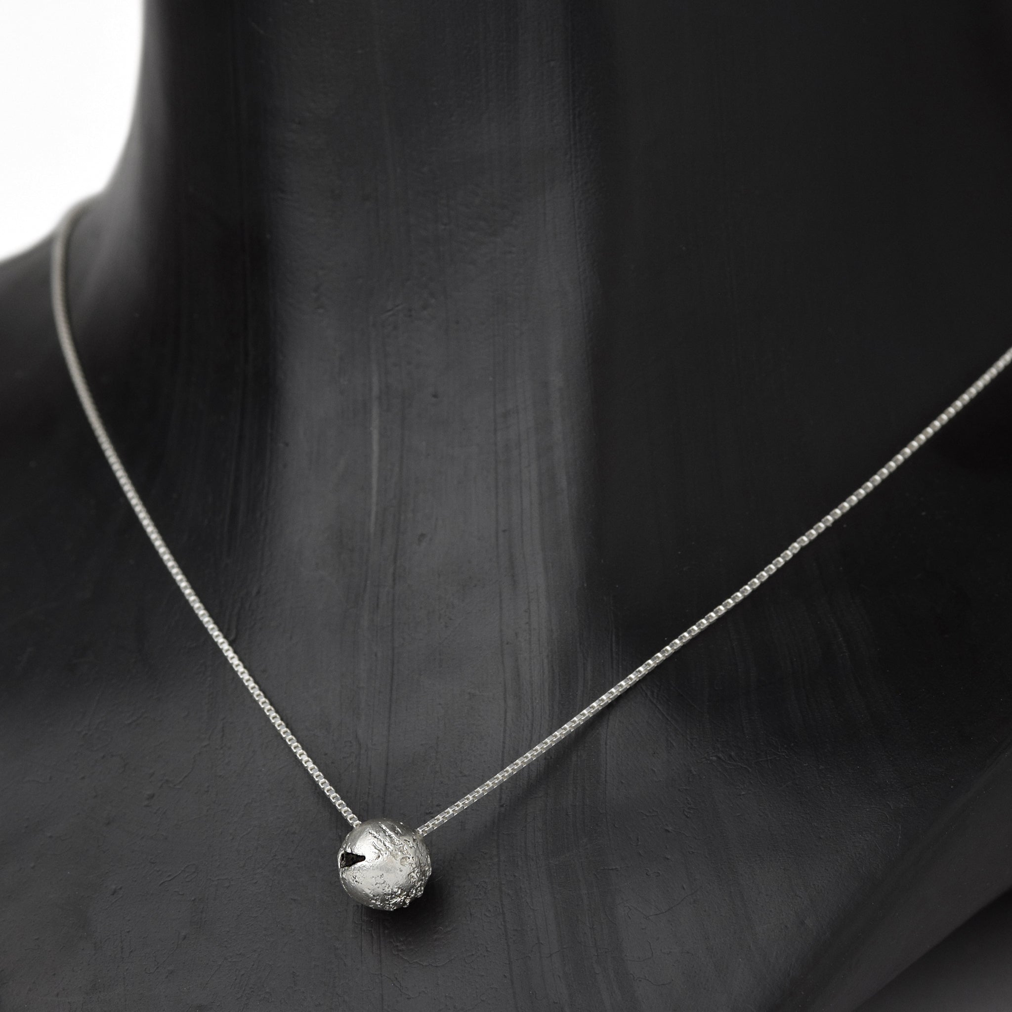 Handcrafted sterling silver hollow sphere pendant with a textured finish suspended from a sterling silver chain on a dark neck.