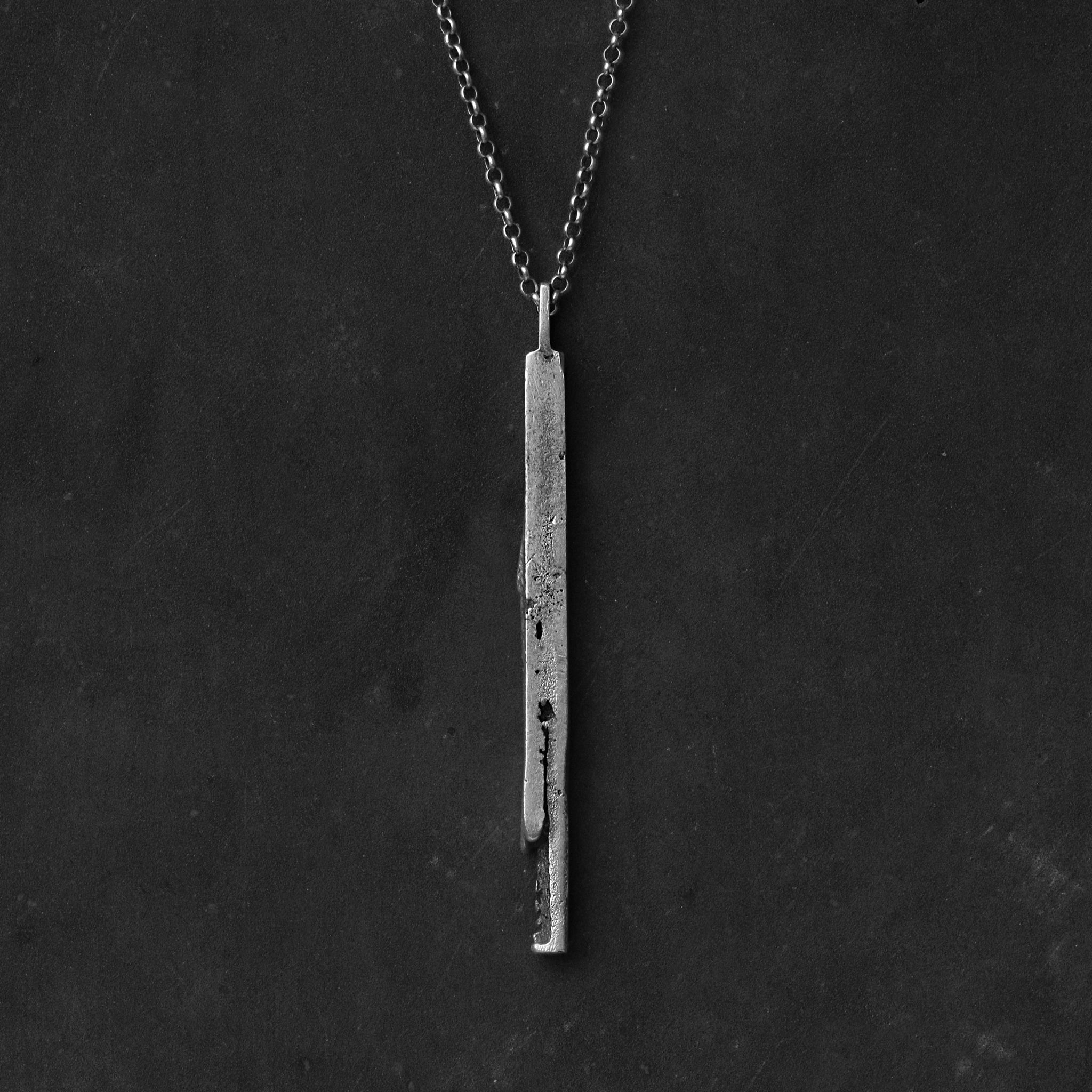 Handcrafted sterling silver bar pendant with a subtle vertical fissure suspended from a sterling silver chain against a black background.