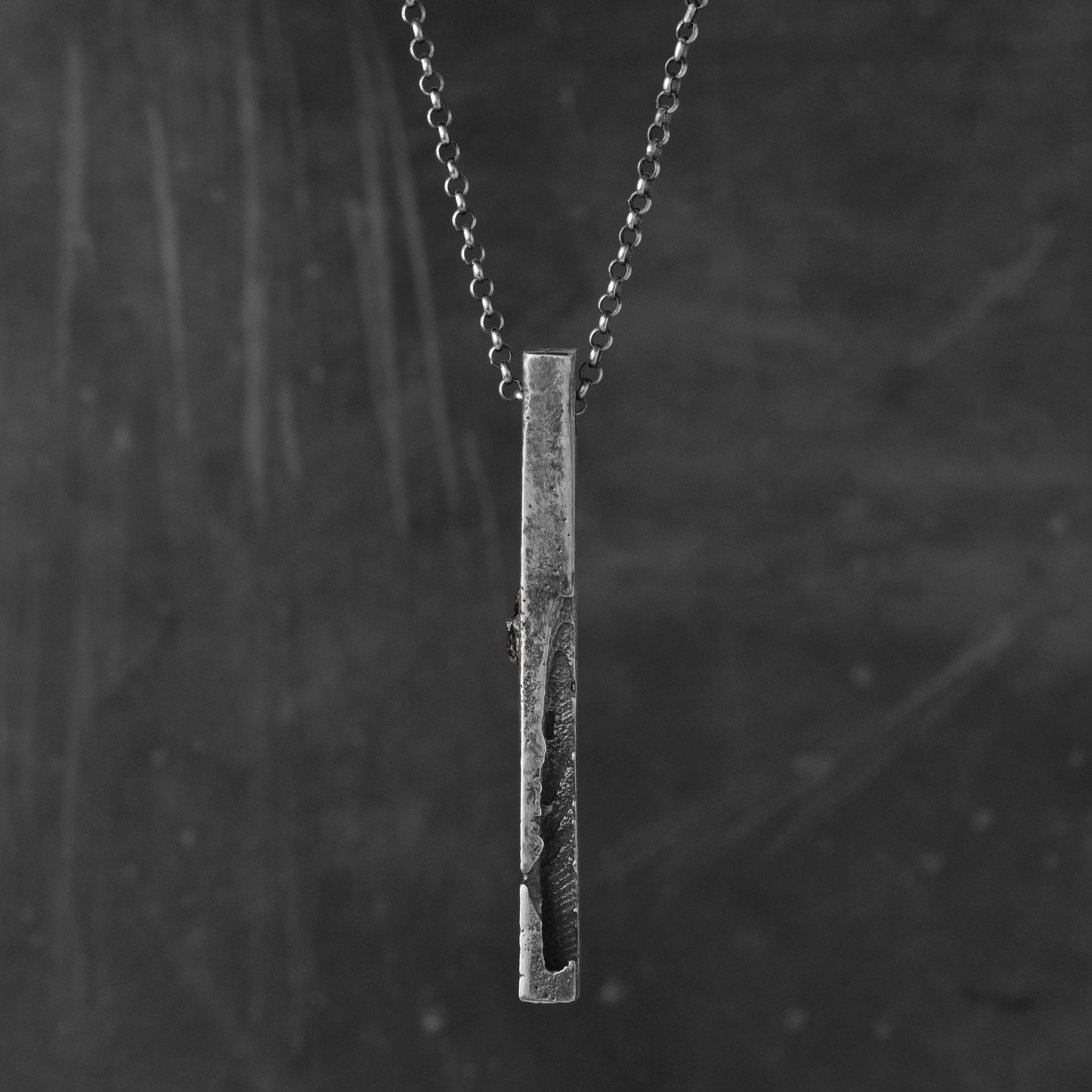 handcrafted sterling silver bar pendant with an silver chain against a dark background.