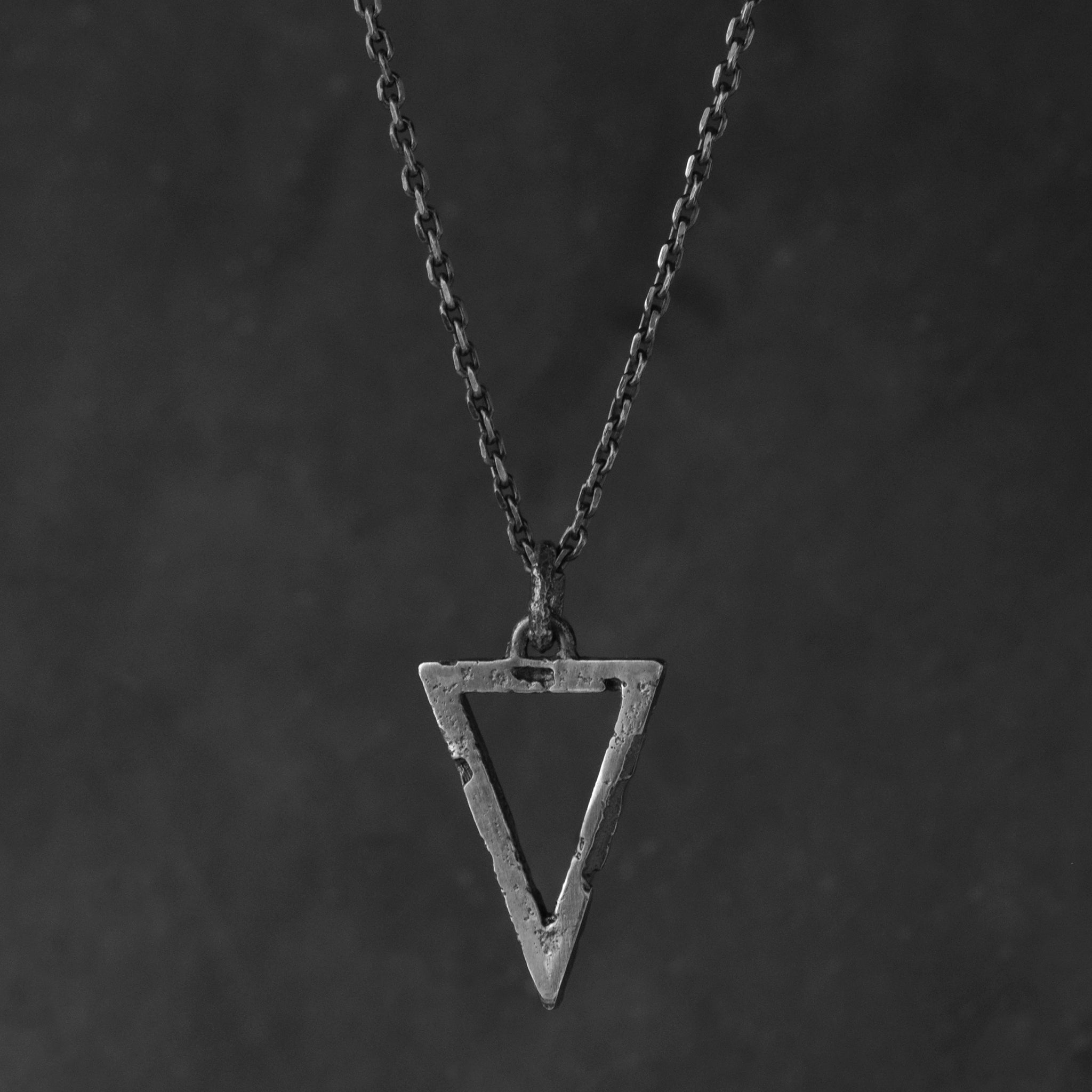 Compact sterling silver triangle pendant with an organic textured finish suspended from a sterling silver chain on a  grey background.